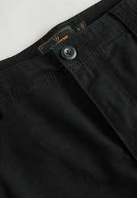 Lähikuva mustista denimhousuista, joissa on vyötärönauha, nappi ja näkyvä oranssi etiketti sisällä.