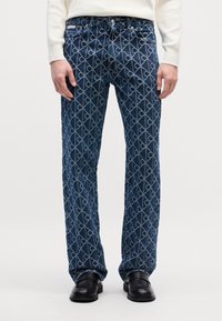 Jeans de mezclilla con un patrón geométrico en tonos azul oscuro y azul claro, corte recto, que cuentan con bolsillos frontales y herrajes metálicos.