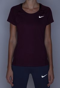 Bordowa sportowa koszulka Nike z krótkimi rękawami i odblaskowym logo na piersi, w zestawieniu z granatowymi legginsami, które również mają logo.