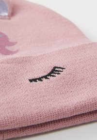 Bonnet tricoté rose avec un détail de broderie cils noirs, texture douce et design lisse et ajusté. Idéal pour un port décontracté.