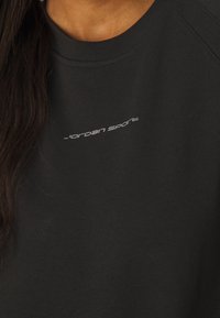 Felpa nera con colletto rotondo e maniche corte. Presenta un piccolo logo bianco "Jordan Sport" sul davanti. Texture morbida e design casual.