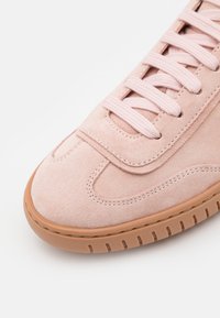 Sneaker in suede rosa con punta rotonda, lacci tono su tono e suola in gomma beige con scanalature testurizzate per una presa migliore. Cuciture decorative lungo le cuciture.