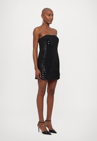 Rochie mini neagră fără bretele, cu o suprafață texturată și paiete reflectorizante. Modelul este asortat cu pantofi cu toc înalt negri și cercei statement.