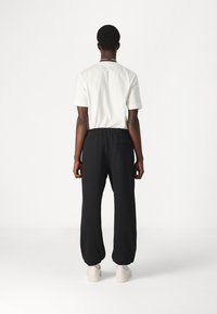 Vit kortärmad skjorta i bomull som är kombinerad med svarta joggers med elastisk midja och elastiska cuffar. Modellen har på sig ljusa sneakers.