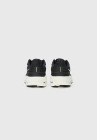 Pantofi sport negri cu un superior texturat, accente albe și un talpă cu amortizare, având un model de cauciuc proeminent, văzuți din spate.