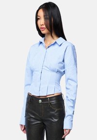 Blau-weiß gestreiftes Crop-Shirt mit spitzem Kragen, Knopfschluss und langen Ärmeln, kombiniert mit schwarzen, schmal geschnittenen Lederhosen.