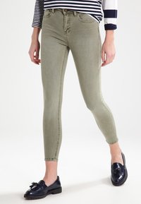 Jeans skinny elásticos de color verde oliva con una textura suave y un diseño clásico de cinco bolsillos, combinados con unos mocasines azul marino.
