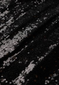 Tela negra cubierta de brillantes lentejuelas plateadas dispuestas en un patrón escalonado, creando una superficie texturizada y reflectante.