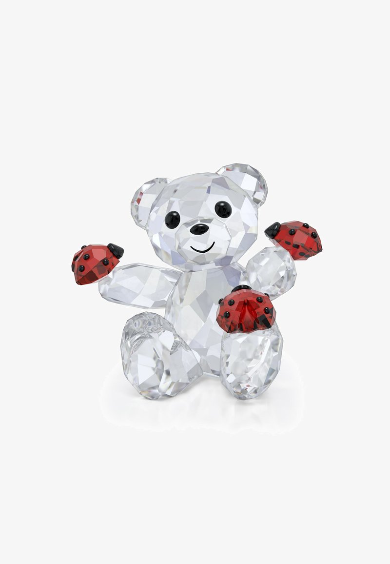 Figúrka medveďa z krištáľu s priehľadnými fasetami, čiernymi očami a usmievajúcimi sa ústami; drží na labkách dve červené lienky s čiernymi bodkami.