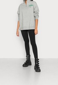 Grå zip-up sweatshirt med grön "Nike" logotyp, som är parat med svarta leggings och svarta kängor med snörning och flera remmar.