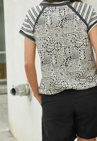 Haut à manches courtes avec un motif géométrique beige et noir, doté d'un col contrastant et d'une bordure de manches assortie, associé à un short noir.