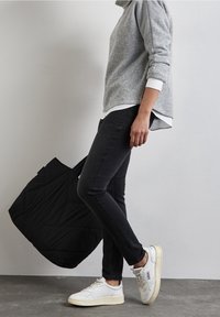 Grå tröja, svarta skinny jeans, vita sneakers och en svart kviltad handväska. Har en avslappnad passform och lager-på-lager-look.