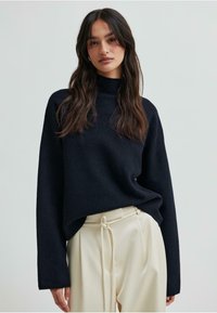 Granatowy sweter z golfem, wykonany z miękkiego materiału, o luźnym kroju i długich rękawach, w zestawie z kremowymi spodniami z plisami.