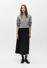 Grå strikket cardigan med knapper, parret med en sort, ankel-længde nederdel. Modellen har grå sokker og sorte loafers på. Simpelt, monokromt design.