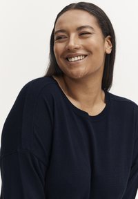 Granatowy sweter dziany z okrągłym dekoltem, charakteryzujący się miękką teksturą i luźnym krojem, z prążkowanymi detalami na rękawach.