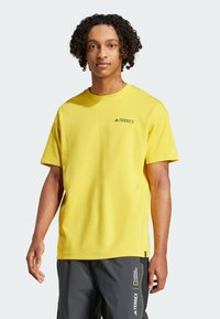 Gul bomull T-skjorte med korte ermer og rund hals. Har en liten svart "TERREX"-logo på brystet. Flat hem-design.