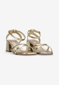 Goldene metallische High-Heel-Sandalen mit einem quadratischen Blockabsatz, ausgestattet mit überkreuzten Riemen und einer glatten Textur auf dem Fußbett.