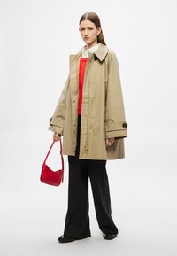 Bézs, nagy méretű esőkabát nagy gallérral, arany gombokkal és zsebekkel, piros pulóver és fekete nadrág fölött rétegezve. Kiegészítve egy piros kézitáskával.