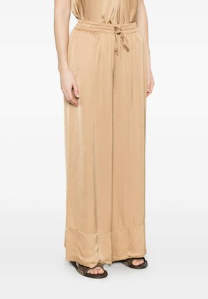 Pantaloni beige a gamba larga con coulisse, indossati con sandali marroni aperti sulle dita, che mostrano la zona dalla vita ai piedi di una persona in piedi.