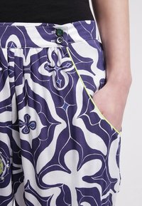 Blå och vit mönstrade byxor med loose fit; har två knäppningar, kontrasterande gul-grön passpoal och en sidficka.