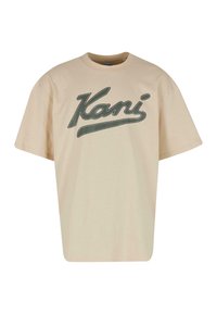 Beige bomulds T-shirt med korte ærmer, der har et stort grønt skriftlogo med teksten "Kani" på forsiden. Enkel, afslappet pasform.