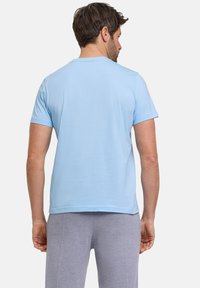 Jasnoniebieska krótki rękaw t-shirt wykonany z miękkiego materiału, z okrągłym dekoltem i prostym dołem. Noszony z szarymi spodniami.