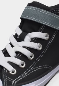 Μαύρο ψηλό αθλητικό παπούτσι με λευκά κορδόνια, γκρι λουράκι με βέλκρο και λευκή ραφή σε λευκή σόλα.