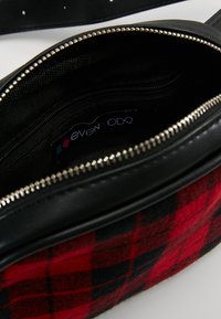Sac en cuir noir avec tissu à carreaux rouge et noir, fermeture éclair en argent et poche intérieure ; dispose d'une étiquette intérieure de marque.