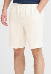 Light beige linen shorts with an elastic waistband, drawstring closure, side pockets, and a relaxed fit, reaching just above the knee.