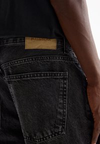 Jeans neri in denim con una finitura testurizzata, dotati di doppie tasche posteriori e di un'etichetta in pelle color cuoio sulla cintura con la scritta "PULL&BEAR" in rilievo.
