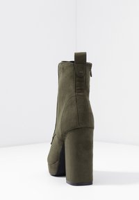 Bottine en suede verte avec un talon bloc haut, dotée d'une boucle à l'arrière, de coutures verticales et d'une fermeture éclair sur le côté.