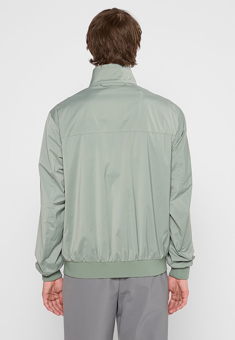 Hellgrüne Zip-Jacke aus glattem, leichtem Material. Verfügt über einen hohen Kragen, elastische Bündchen und einen gesäumten Saum.