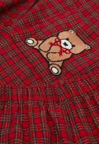 Rødternet kjole med samlet elastik i taljen. Har en broderet brun bjørn med et rødt bånd. Blødt, struktureret bomuldsstof.