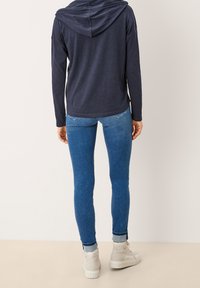 Námořnicky modrá mikina s volnějším střihem, s kapucí na stahovací šňůrce, doplněná světle modrými úzkými džínami a bílými kotníkovými botami.