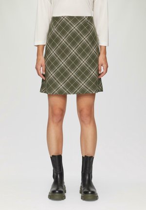 Grønternet nederdel med en udvidet silhuet, der har hvide og mørkegrønne linjer. Kombineret med sorte ankelstøvler.