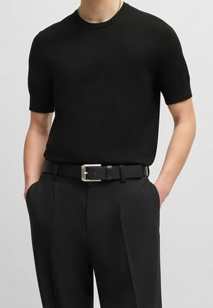 Suéter negro de manga corta con textura suave, combinado con pantalones negros de corte ajustado y un cinturón negro con hebilla plateada.