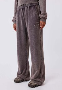 Joggers de terciopelo gris con un corte relajado, que cuentan con bolsillos laterales y un logo "PXP" en blanco. Textura suave con un aspecto ligeramente desgastado.