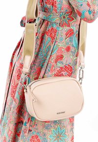 Borsa a tracolla in finta pelle rosa chiaro con superficie testurizzata e chiusura con zip, dotata di una resistente tracolla beige regolabile.