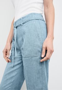 Ljusblå denimbyxor med en avslappnad passform, utrustade med dragsko i midjan, sidfickor och subtila texturdetaljer på tyget.