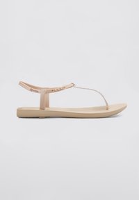 Sandalias planas de color beige claro, hechas de plástico suave, con una tira entre los dedos y un acento decorativo en plata, con suela plana y sin tacón.