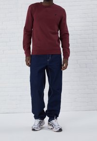 Felpa bordeaux con collo rotondo, polsini a costine, abbinata a jeans larghi blu scuro, completata da scarpe sportive argentate.