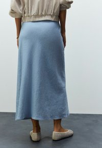 Fustă de lungime medie, de culoare albastru deschis, realizată dintr-un material texturat, având un design evazat. Asortată cu pantofi plat țesuți de culoare bej.