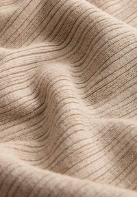 Bež pletena tkanina z navpično rebrasto teksturo, prikazana v mehkih gubah in podrobnem posnetku.