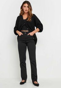 Svart stickad cardigan med överdimensionerade ärmar, tillsammans med en svart kort topp och höga svarta byxor. Skor: svarta ballerinas.