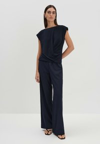 Top drappe navy blue con maniche a cappuccio, abbinato a pantaloni a gamba larga dello stesso colore. Tessuto liscio con una leggera lucentezza. Design sofisticato.