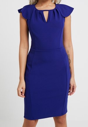 Dopasowana królewsko niebieska sukienka do kolan z falbanowymi rękawkami i dekoltem z wycięciem na szyi, noszona przez osobę z widocznymi tatuażami na ramionach.