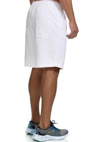Pantalones cortos de algodón blancos con una cintura elástica, que cuentan con un bolsillo lateral y un diseño limpio. Combinados con zapatillas deportivas grises.