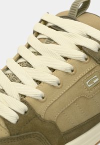 Sneaker din suede bej cu şireturi crem și accente din plasă, având un logo distinct și un toc texturat pentru un plus de detaliu.