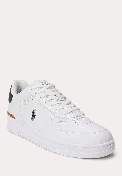 Bela nizka superga z luknjicami na sprednjem delu, črnim logotipom Polo na strani, belimi vezalkami in črnim jezičkom na peti, prikazana na svetli podlagi.