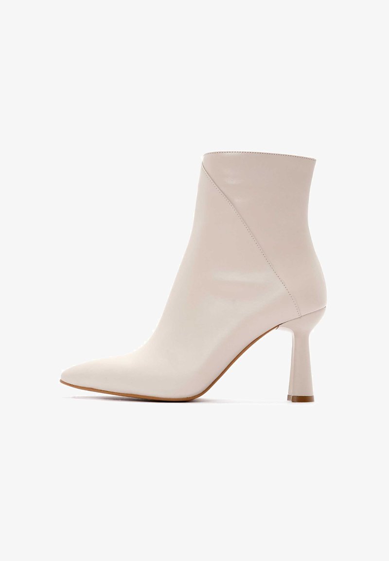 Botín de tobillo con punta afilada en cuero beige claro suave, que presenta un diseño elegante y un tacón de aguja con un detalle de costura minimalista.